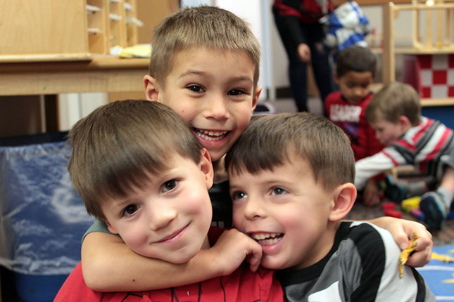 three UNO Child Care Center students smiling and hugging each other